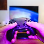 Close-up of hands holding a game controller in front of a TV screen. Perfect for entertainment setups. — Direct Baccarat Webs